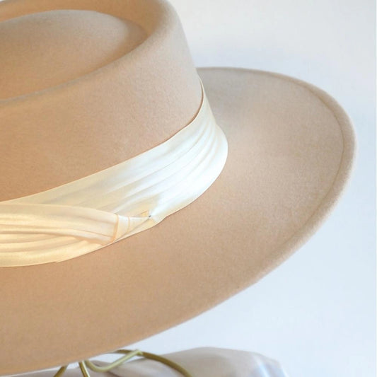 A close up side view of the beige beauty wool satin lined boater hat with the ivory satin hat band.