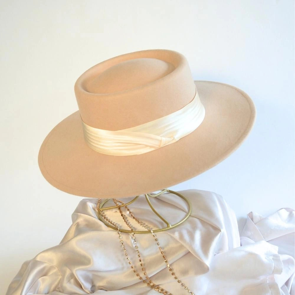 A side view of the beige beauty wool satin lined boater hat with the ivory satin hat band.