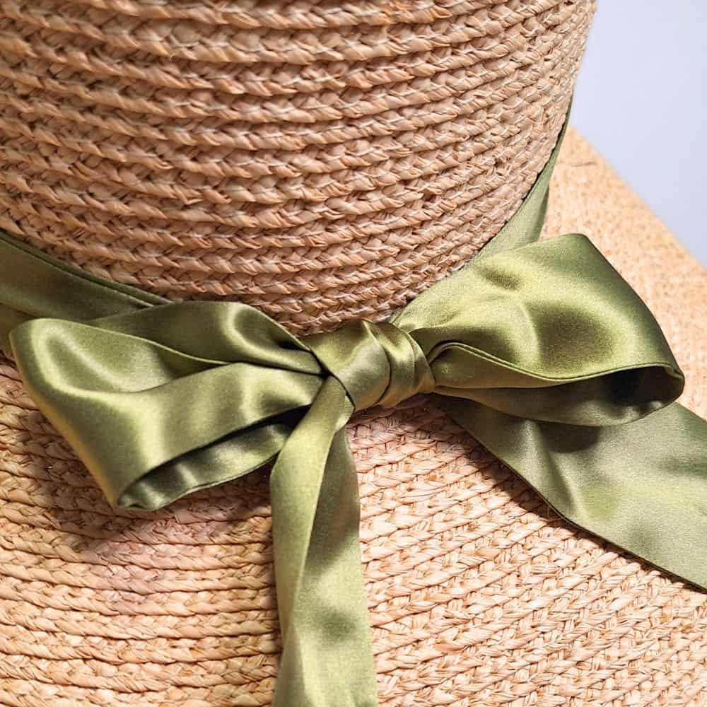 A close up view of the olive green bow on our raffia straw satin lined beach hat, perfect for curly and textured hair.