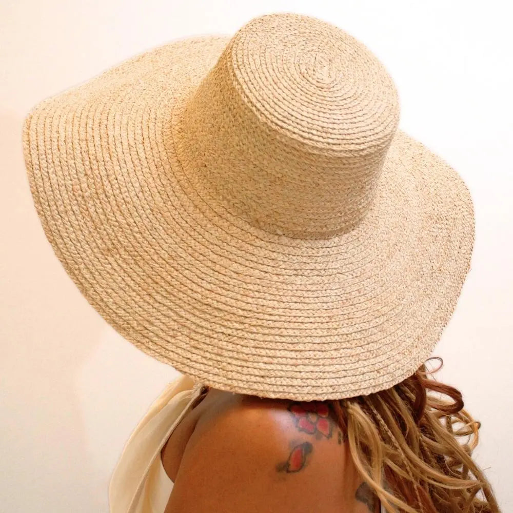 Back view of model wearing sunlit dream satin lined wide brimmed raffia sun beach hat.