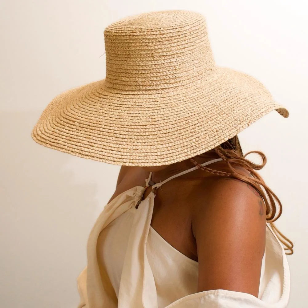 Side view of model wearing sunlit dream satin lined wide brimmed raffia sun beach hat.